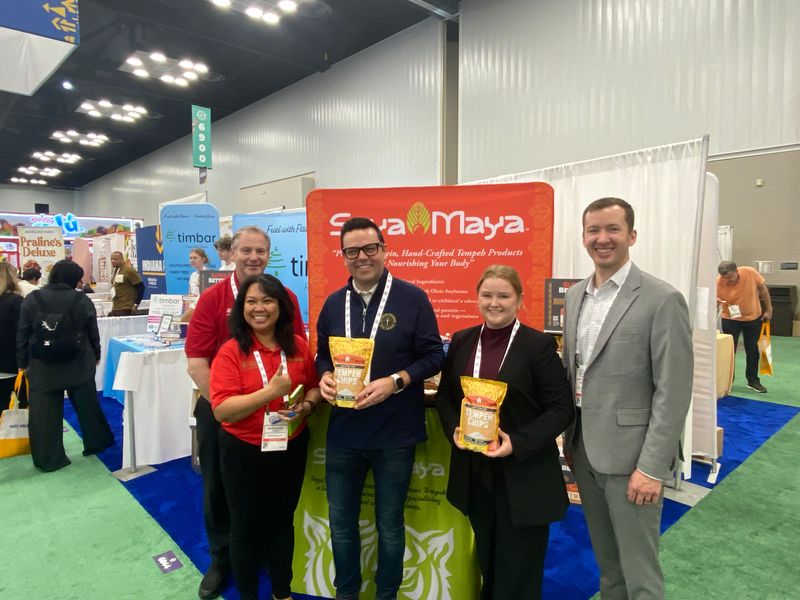 “how to make a tangy garlic seasoning, group photo of Soya Maya representatives showcasing their tangy garlic seasoned tempeh chips at a trade show”.