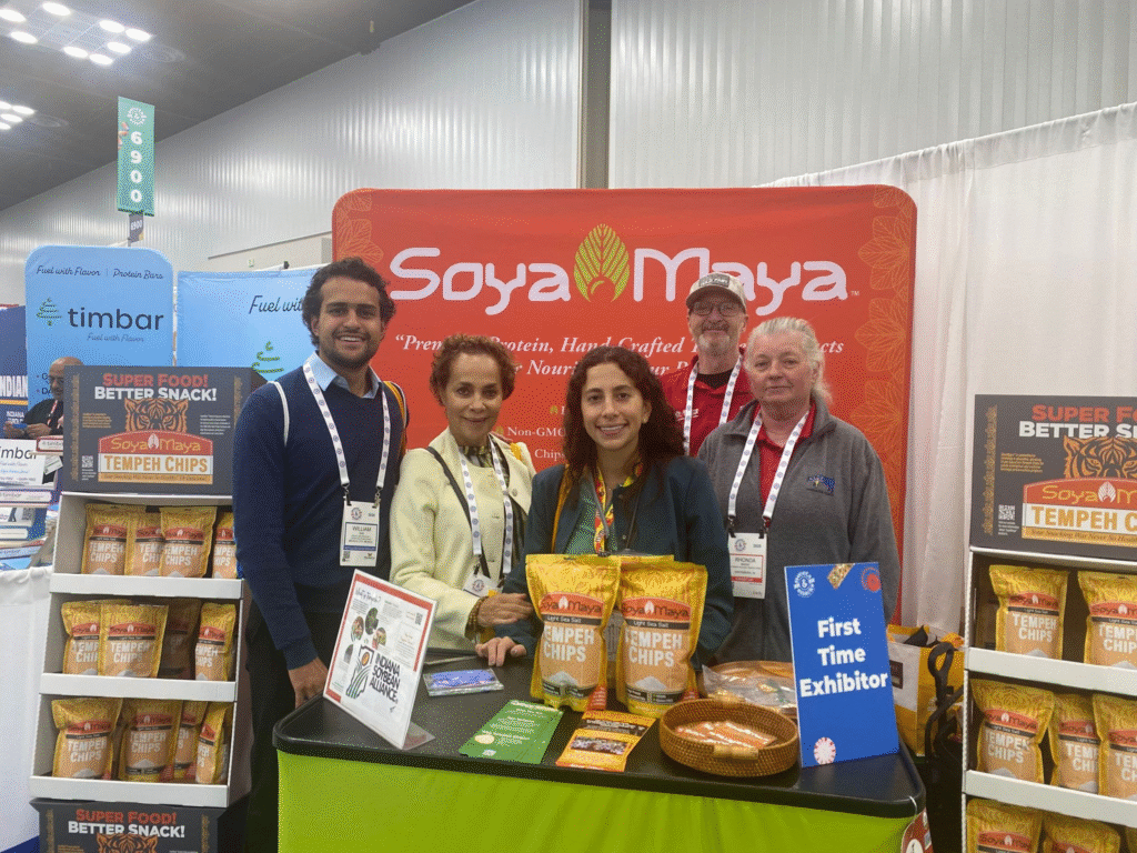 “what are tangy garlic Soya Maya's booth at an event, showcasing their Tangy Garlic Tempeh Chips and other vegan, non-GMO snack products”.
