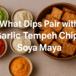 “Assortment of dips including pesto, creamy sauce, and orange-colored dip alongside fried tempeh chips”.