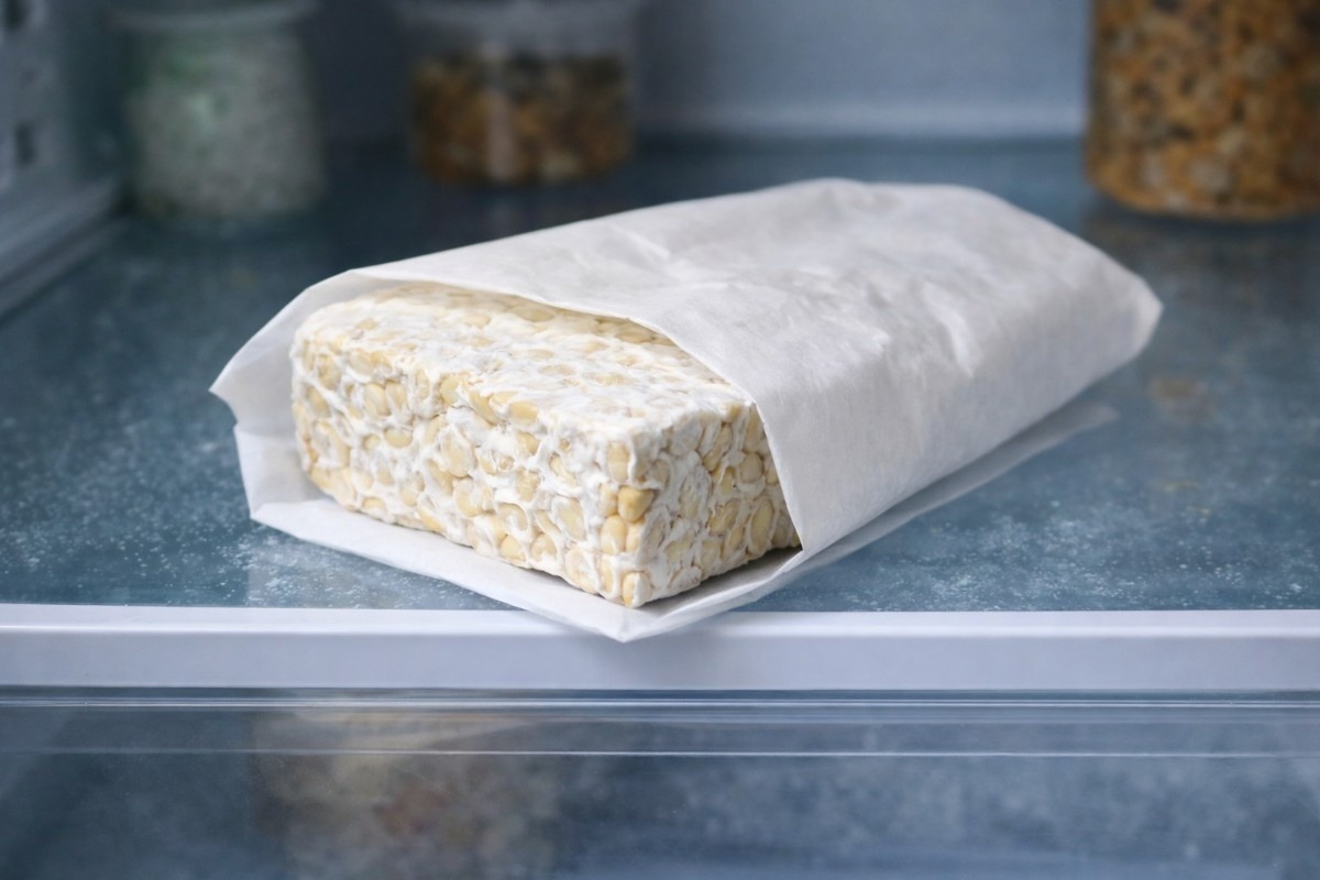 How to Store Tempeh properly, showing fresh tempeh wrapped in paper and stored on a clean refrigerator shelf.