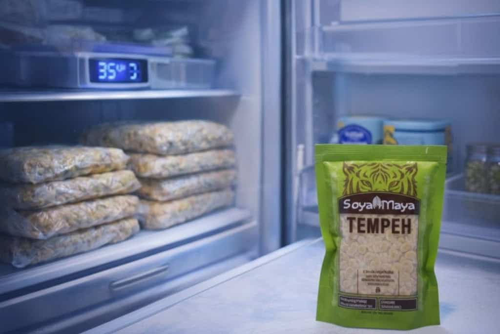 Soya Maya Tempe in a green package on a refrigerator shelf with stored tempeh blocks.
