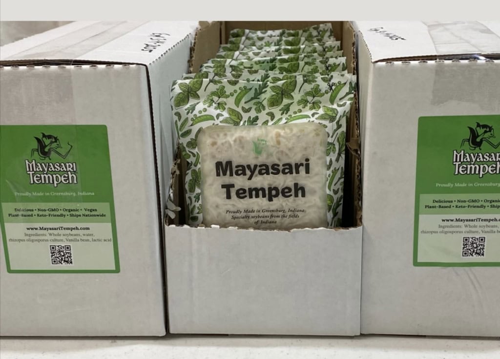 A box filled of Mayasari Tempeh as non-GMO tempeh with green packaging.