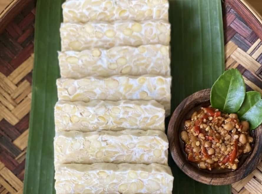 Sliced traditional Indonesian tempeh on banana leaf with sambal, representing the benefits of live culture tempeh