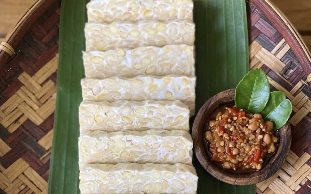 Sliced traditional Indonesian tempeh on banana leaf with sambal, representing the benefits of live culture tempeh