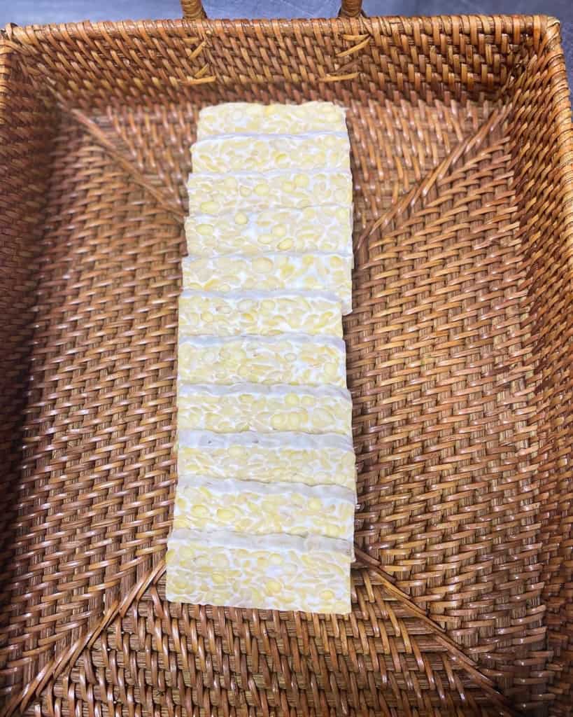 Sliced tempeh blocks in a wicker basket displaying how does tempeh fermentation work by binding beans with white mold