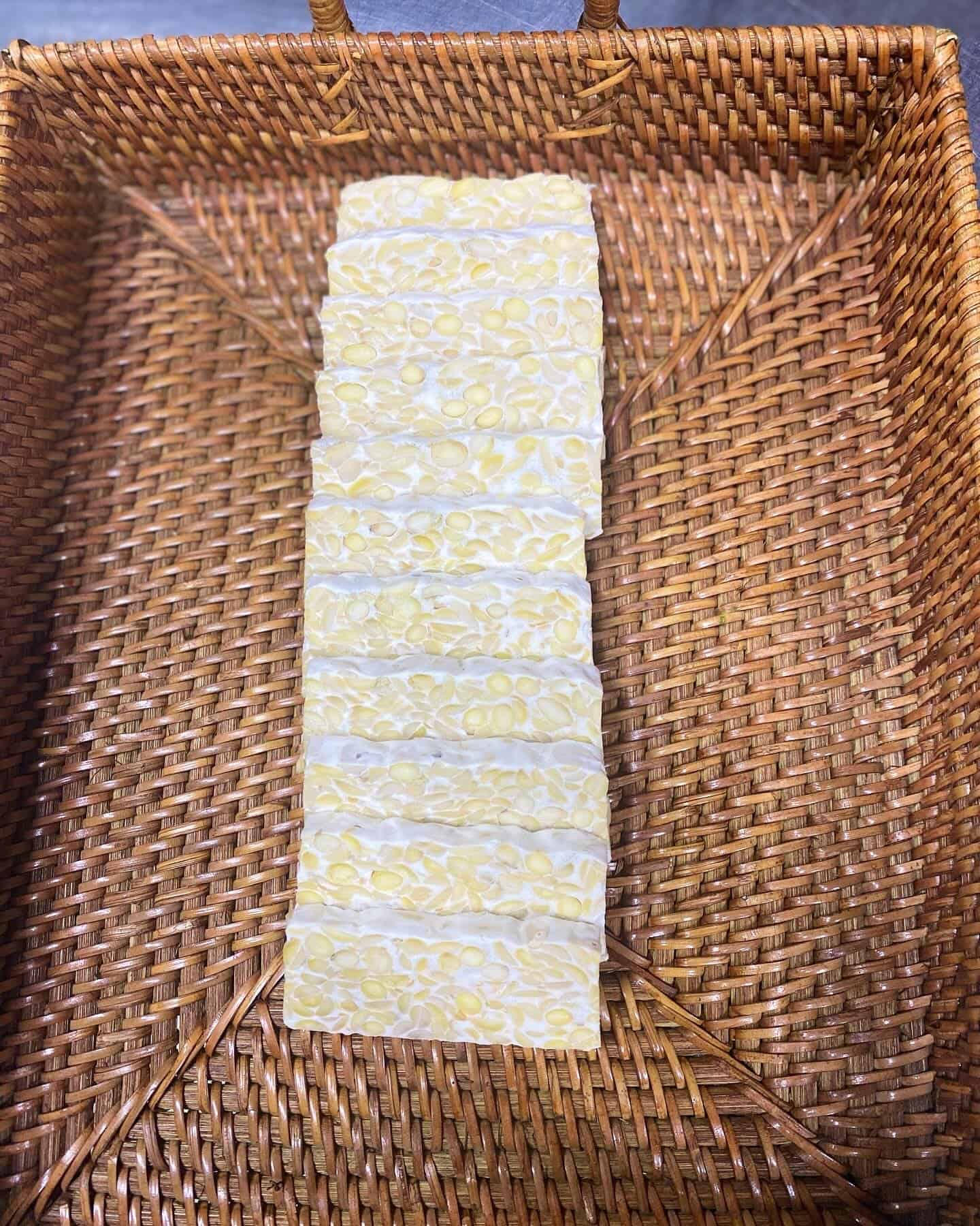 What is rhizopus oligosporus culture result: freshly fermented tempeh slices with white mycelium in a woven basket.