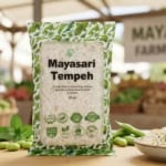 Packaged Mayasari Tempeh on a market stall with fresh vegetables in the background.