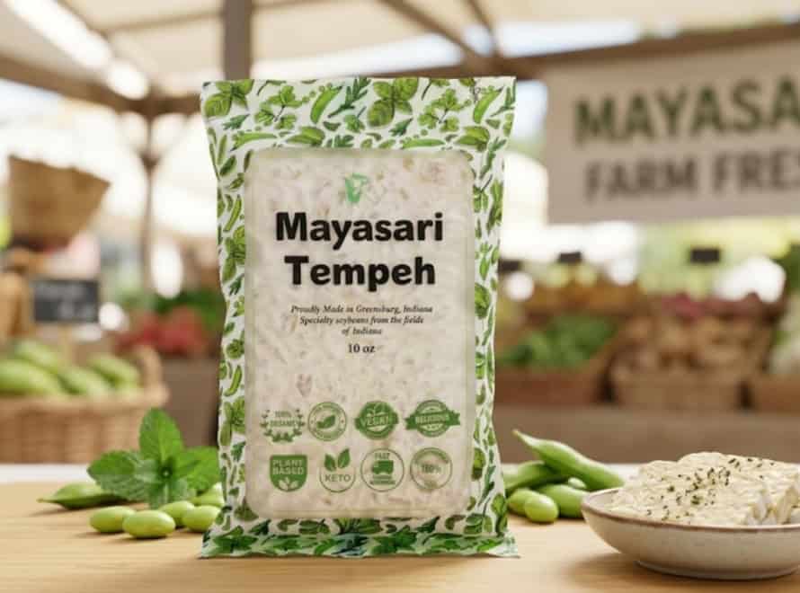Packaged Mayasari Tempeh on a market stall with fresh vegetables in the background.