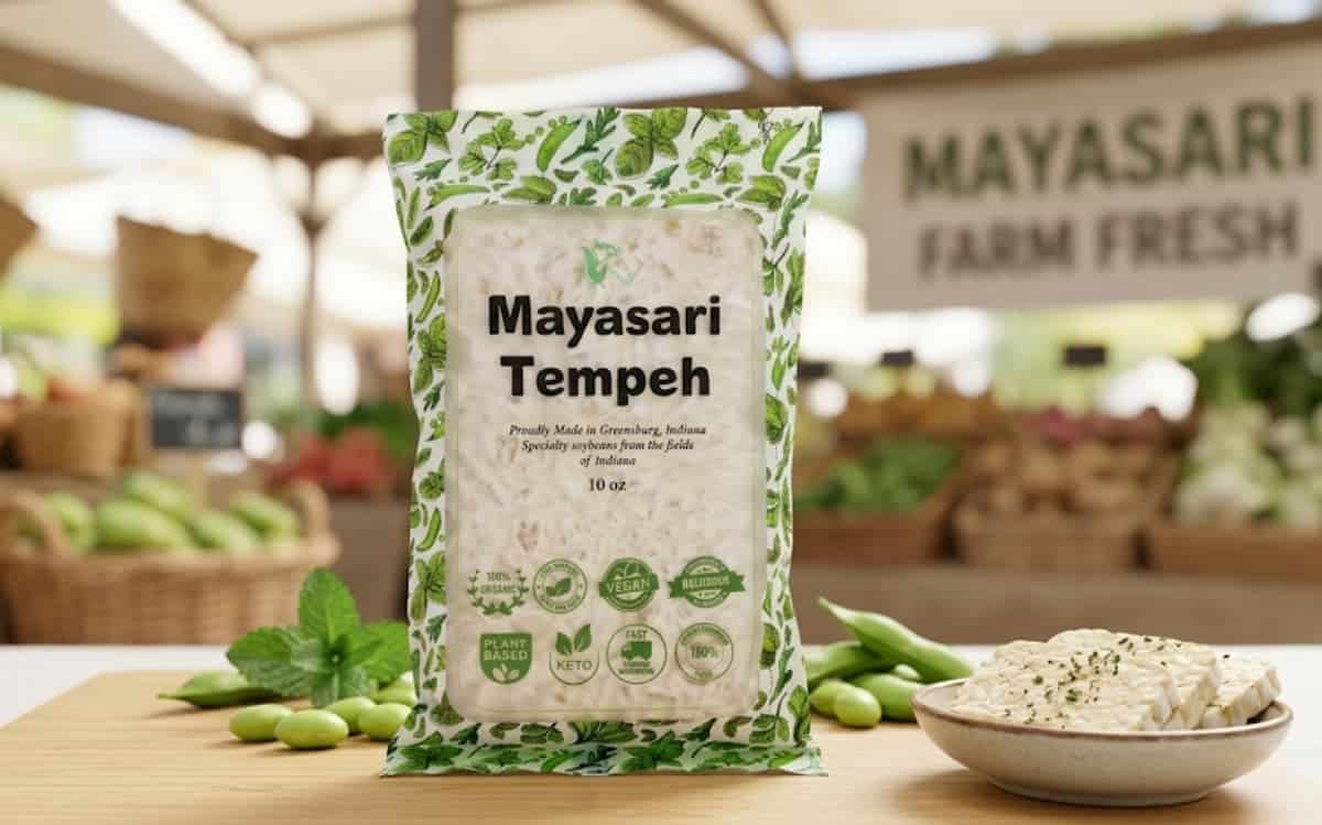 Packaged Mayasari Tempeh on a market stall with fresh vegetables in the background.