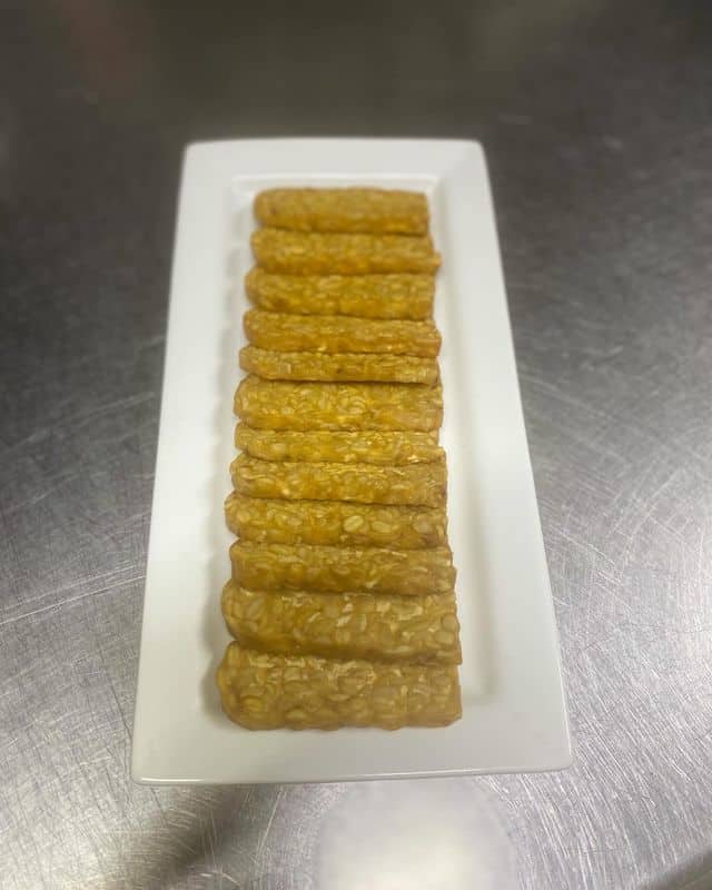 Sliced fried tempeh on white plate, honoring who invented tempeh fermentation as Indonesia's protein staple.
